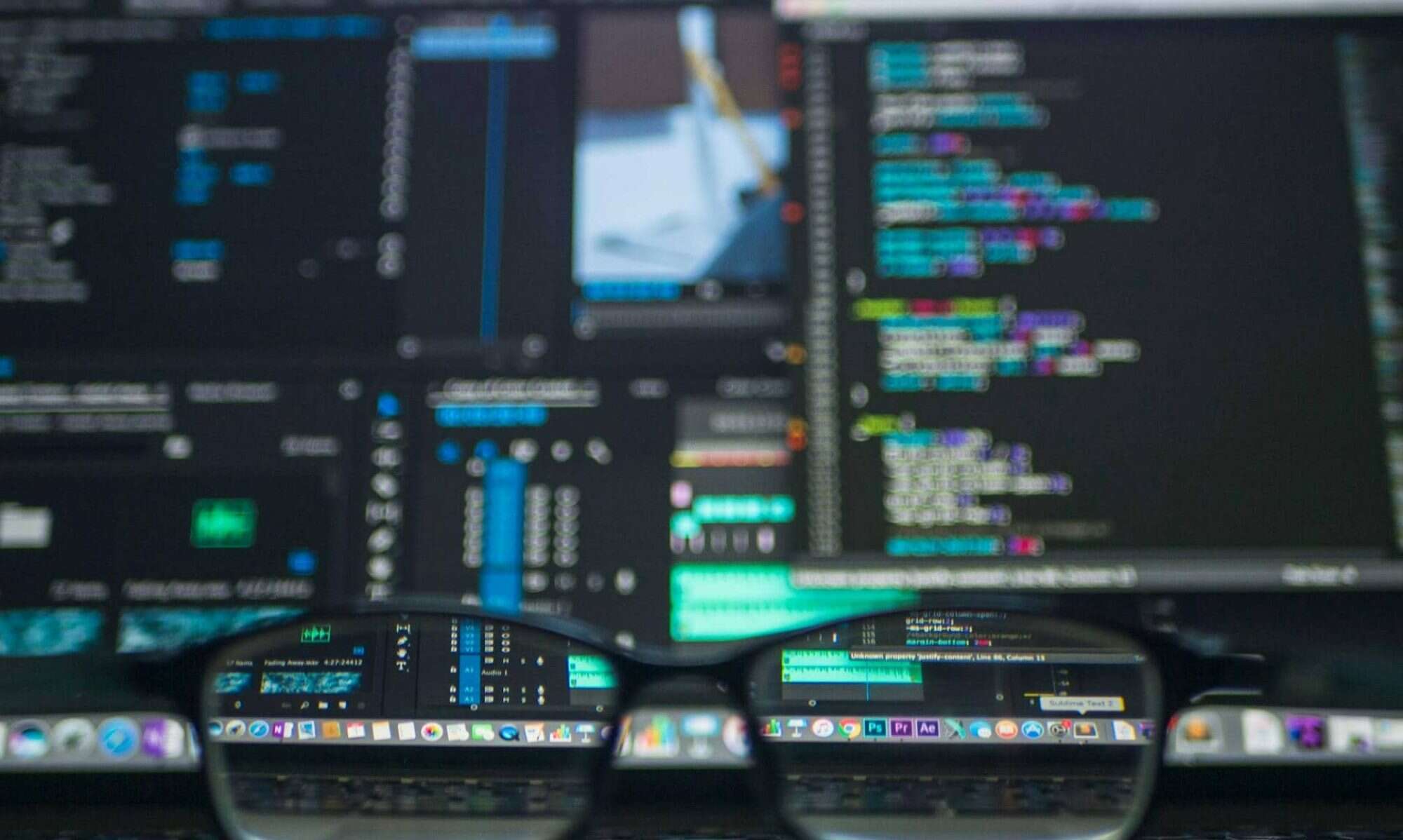 AI Office Developers - Coding on dual monitors, software development, programming, tech office setup, developer work station, IT coding environment. Colorful coding screens displayed on dual monitors with glasses in forefront, highlighting AI office developer activities.